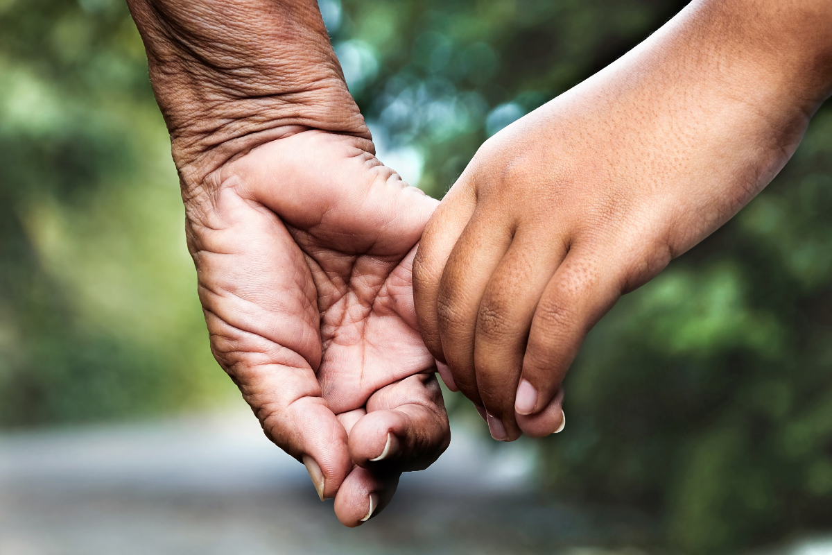 old indian ladys hand holding a childs hand, walking down a road with greenery on ecah side